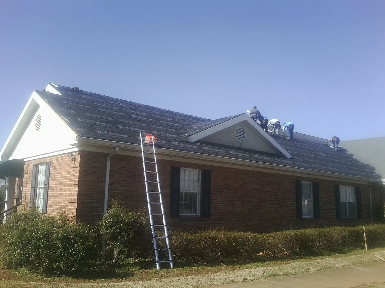 Crew tearing shingles off a brick ranch roof with a ladder set — Metal Roof Repair work by our crew in Holyoke