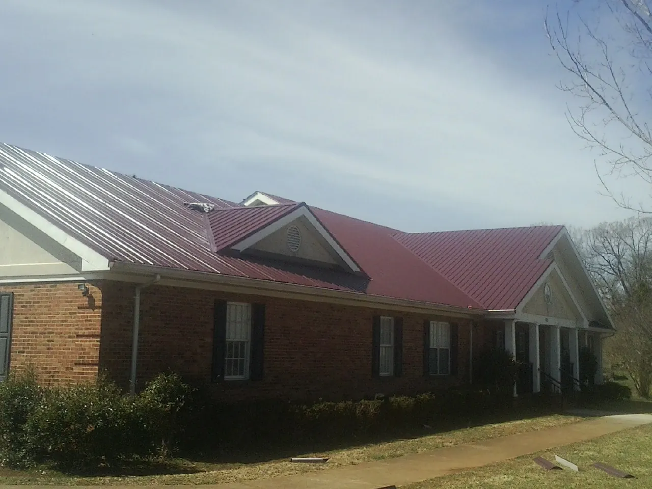 Red metal roof with gabled entries on a long brick building, from a Hail Damage Roof Repair job in Holyoke