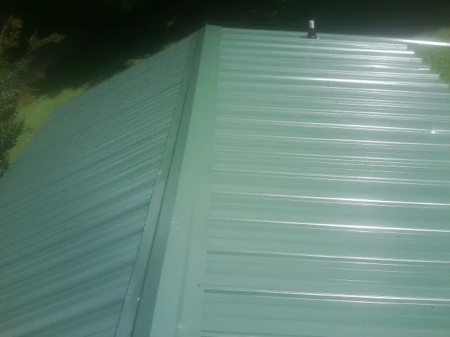 New green metal panels meeting at the ridge of a roof — Flat Roof Repair work by our crew in Holyoke