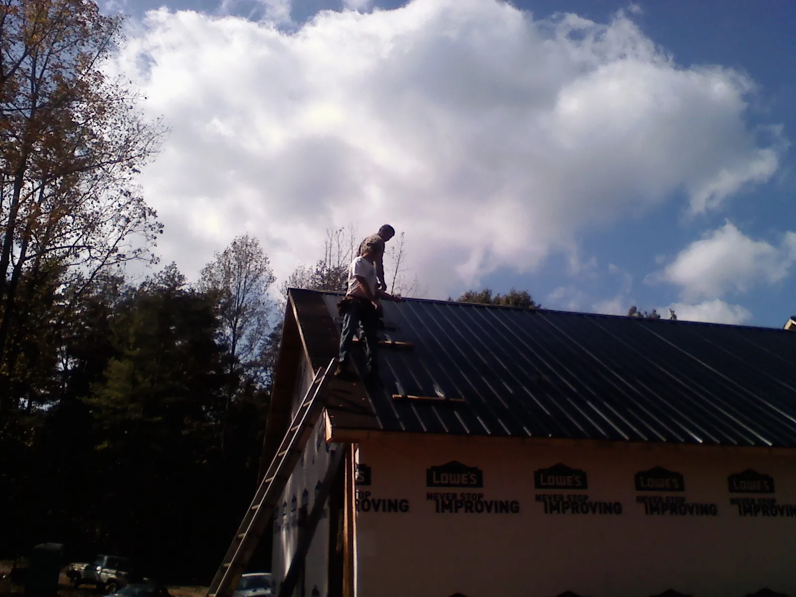 Roofer fastening dark metal panels high against a cloudy sky, from a Roof Inspection job in Holyoke